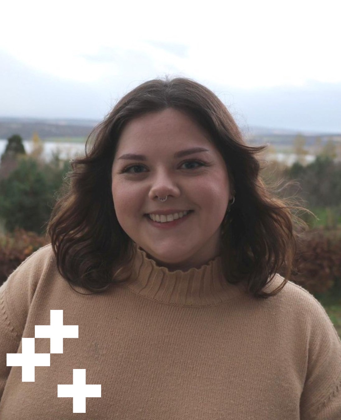 A headshot of Alanna Magee-Shamaan, Marketing Assistant at UHI Moray. She has dark brown hair, shoulder length, is smiling at the camera and wearing a beige turtle neck top