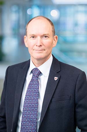 Roger Sendall, Deputy University Secretary, in formal business attire picture against a blue backdrop at An Lochran on Inverness Campus