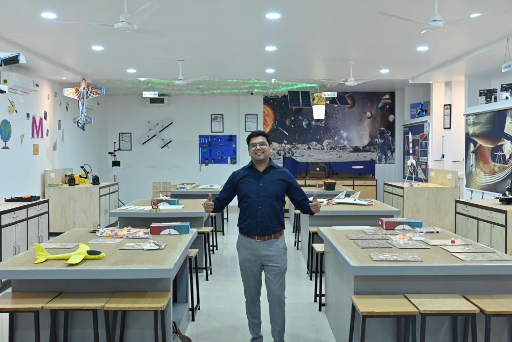 Ashish Kumawat standing in a classroom with his thumbs up
