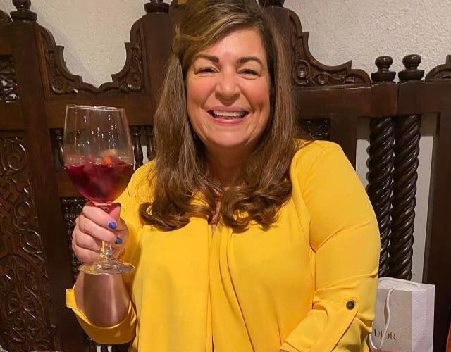 Helen MacDonald holding a wine glass, wearing a yellow blouse