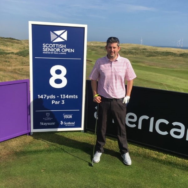Callum Taylor standing on a golf course with 'Scottish Senior Open' sign behind him, at hole 8