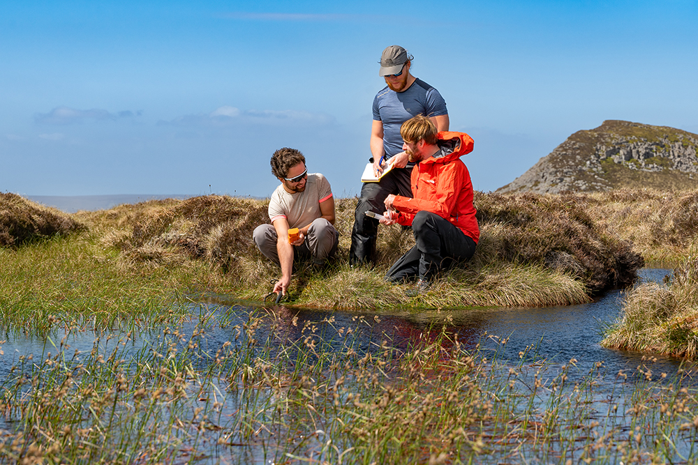 Three people taking a water sample in a peat bog