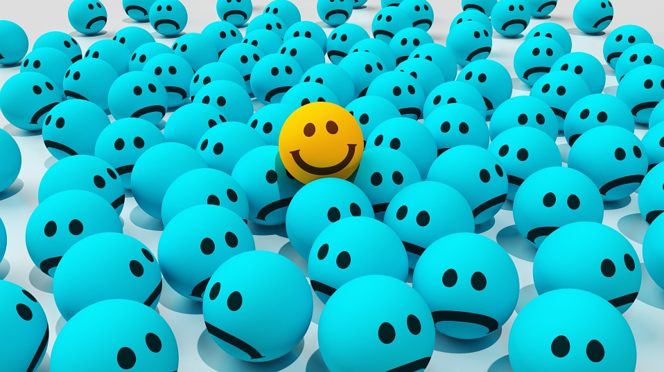 A yellow happy face amongst blue sad faces