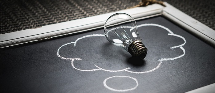 A lightbulb on top of a blackboard on which is drawn a thought bubble