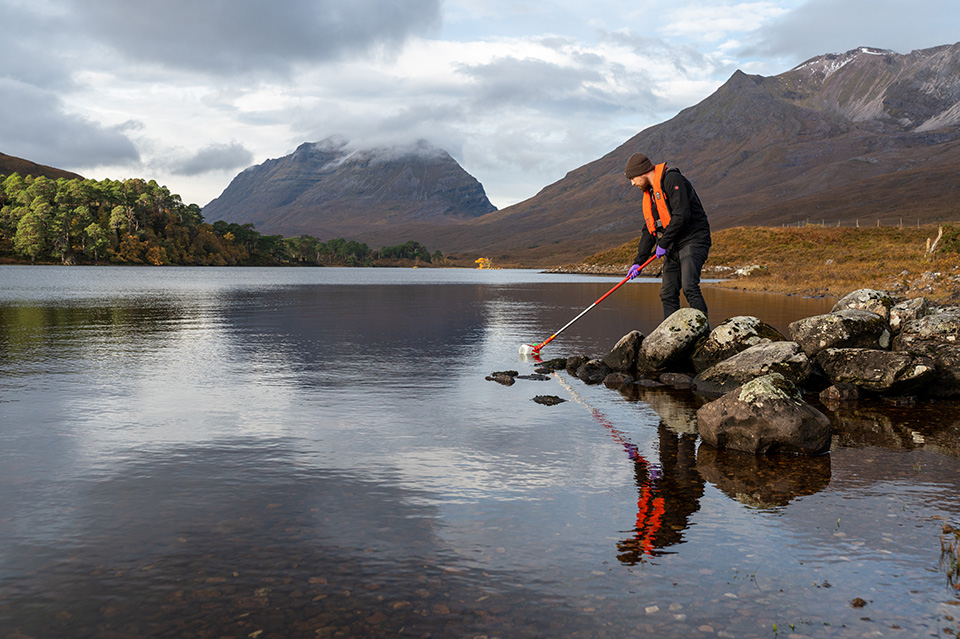 Person taking a water sample in a mountainous region