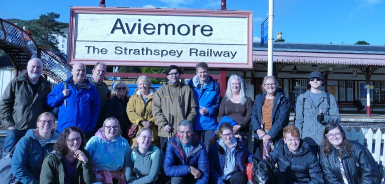 Group of people and a dog posing in front of a sign saying Aviemore.