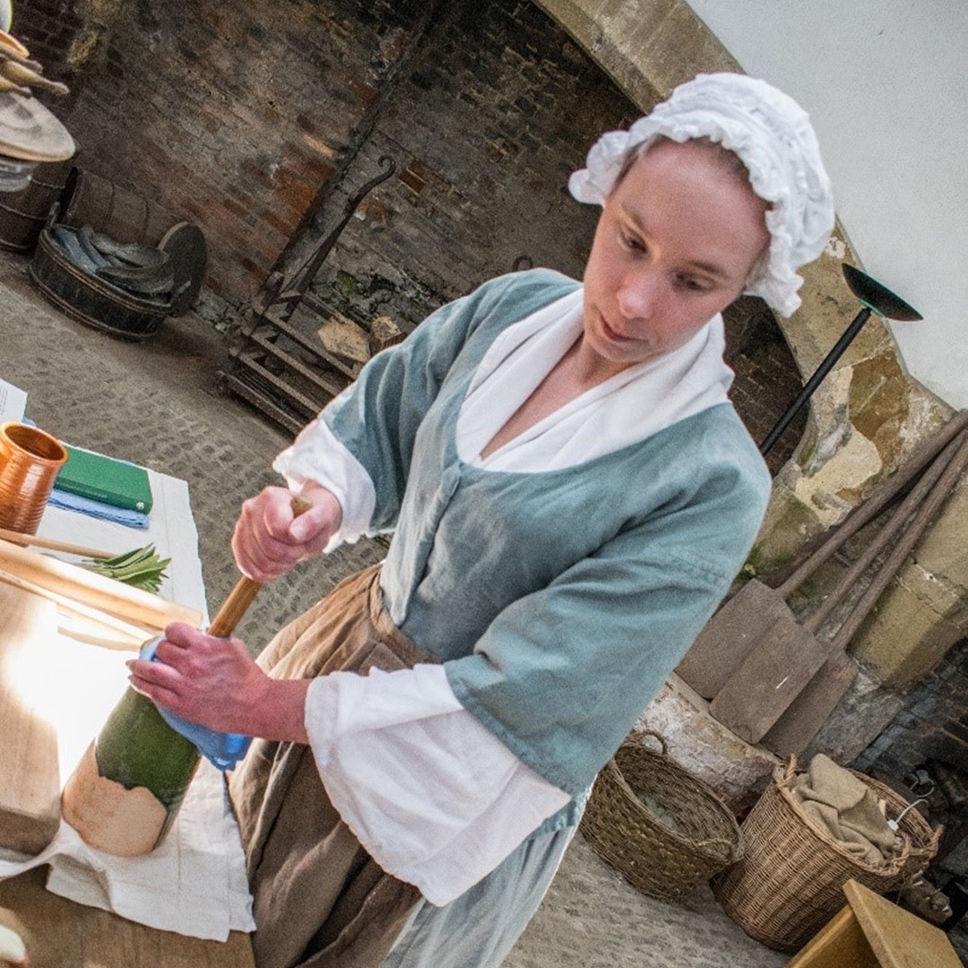 Woman wearing a period costume, photographed in a kitchen setting