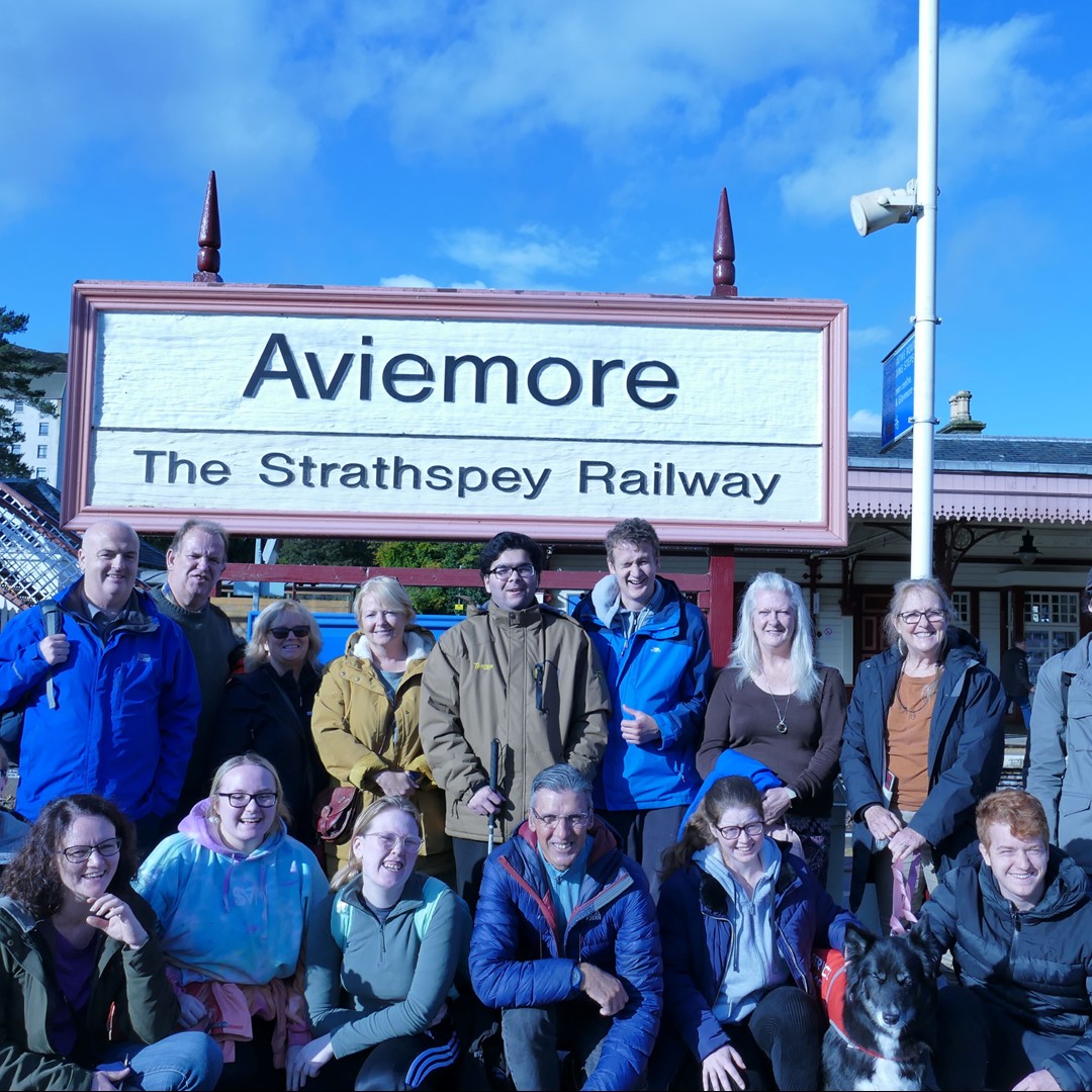 Group of people standing in front of a sign that says Aviemore.