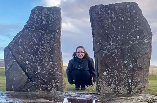 Mila crouching at the Stones of Stenness, Orkney